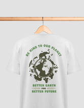 Das Bild zeigt ein weißes T-Shirt, das an einem Holzbügel hängt. Auf der Rückseite des T-Shirts befindet sich ein grüner Aufdruck mit einem Umweltschutzmotiv. In der Mitte ist eine Darstellung der Erde umgeben von Silhouetten verschiedener Tiere, darunter ein Nashorn, ein Löwe, Vögel und Schmetterlinge. Oben steht der Text "BE KIND TO OUR PLANET" in einem Bogen, und darunter "BETTER EARTH FOR BETTER FUTURE". Die Schrift ist ebenfalls in grün gehalten.