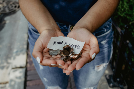 Zwei Hände halten Münzen und einen Zettel mit der Aufschrift "Make a change"