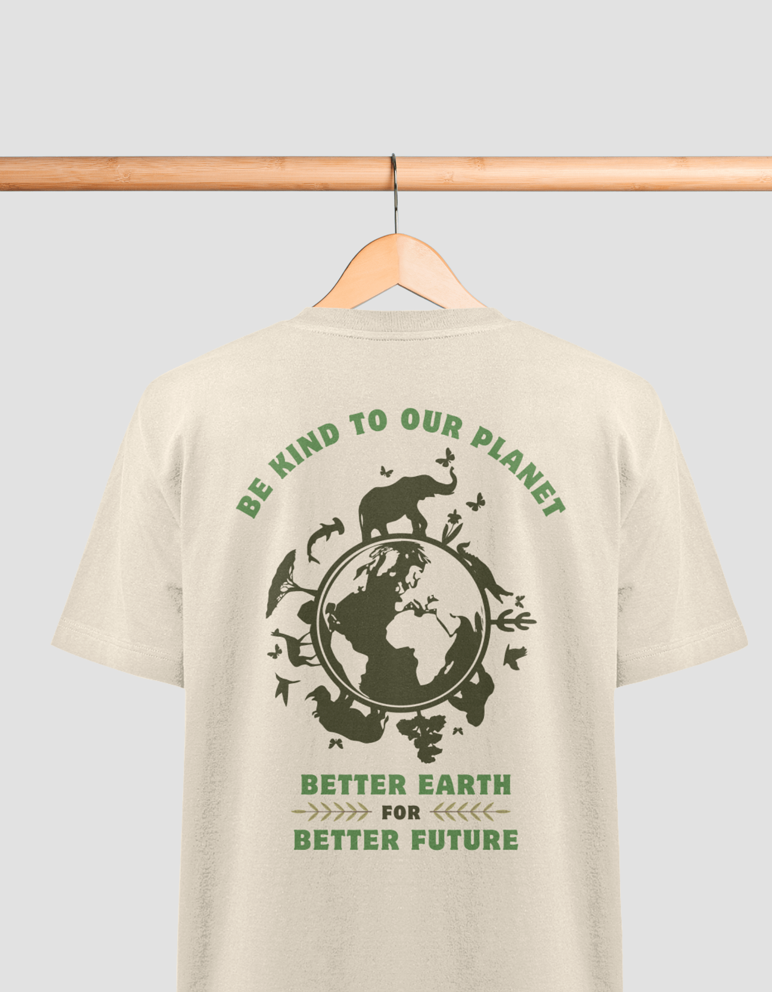 Das Bild zeigt ein beiges T-Shirt, das an einem Holzbügel hängt. Auf der Rückseite des T-Shirts befindet sich ein grüner Aufdruck mit einem Umweltschutzmotiv. In der Mitte ist eine Darstellung der Erde umgeben von Silhouetten verschiedener Tiere, darunter ein Nashorn, ein Löwe, Vögel und Schmetterlinge. Oben steht der Text "BE KIND TO OUR PLANET" in einem Bogen, und darunter "BETTER EARTH FOR BETTER FUTURE". Die Schrift ist ebenfalls in grün gehalten.